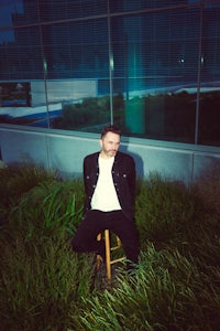 a man sitting on a stool in front of tall grass