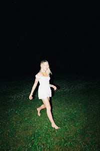 a woman in a white dress running through a field at night
