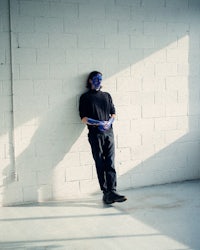 a man leaning against a wall with blue paint on his face